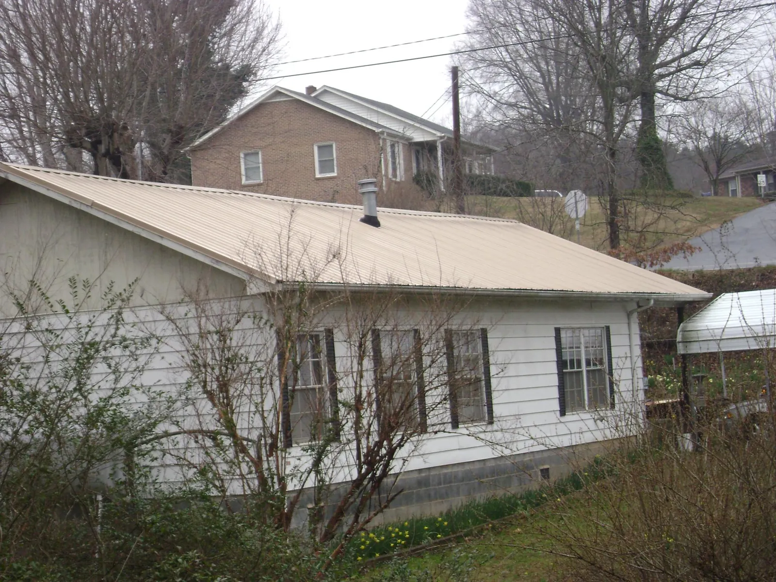 Tan metal roof on a white sided house set into a hillside — Commercial Roofing by Roofing Brothers in Fox Lake